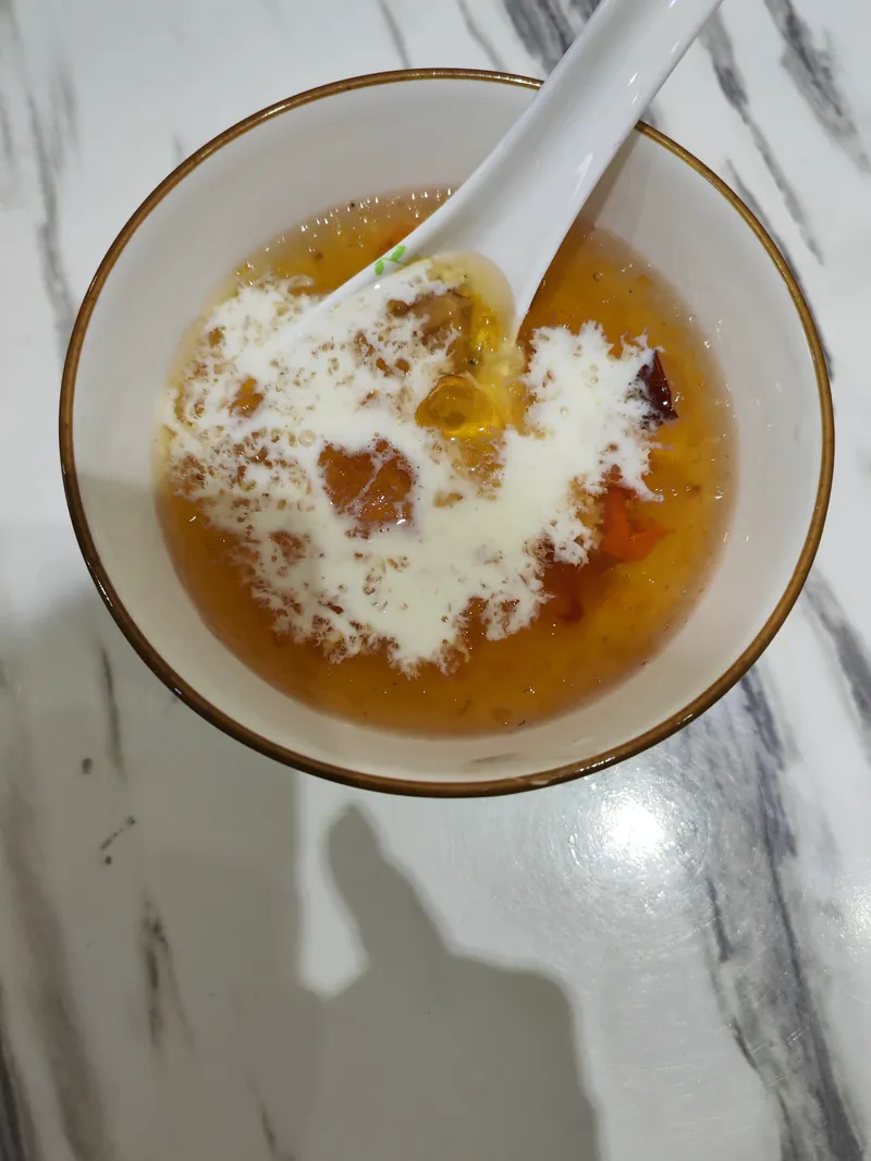 白碗里的桃胶雪燕牛奶，金黄的桃胶上淋着牛奶，旁边一颗红枣，俯拍。
