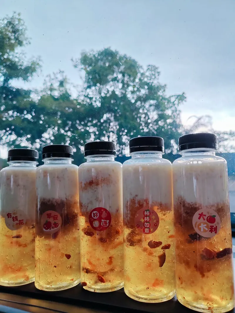 五瓶桃胶雪燕牛奶排在窗边,贴着有钱花、平安、好運连连、柿柿如意、大吉大利。